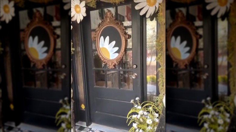 Black glass front door with ornate frame and chalkboard with daisy art and matching foliage