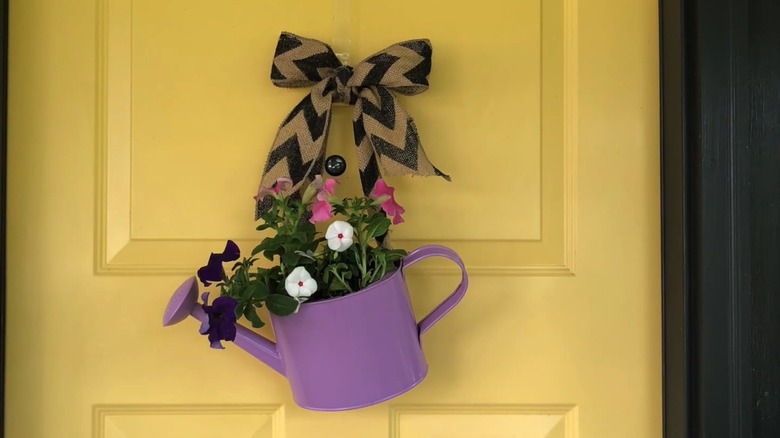 Bright yellow front door with watering can decoration hanging under a bow