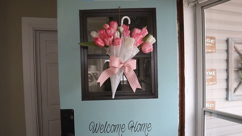 Teal front door decorated with umbrella filled with flowers with a large bow on it