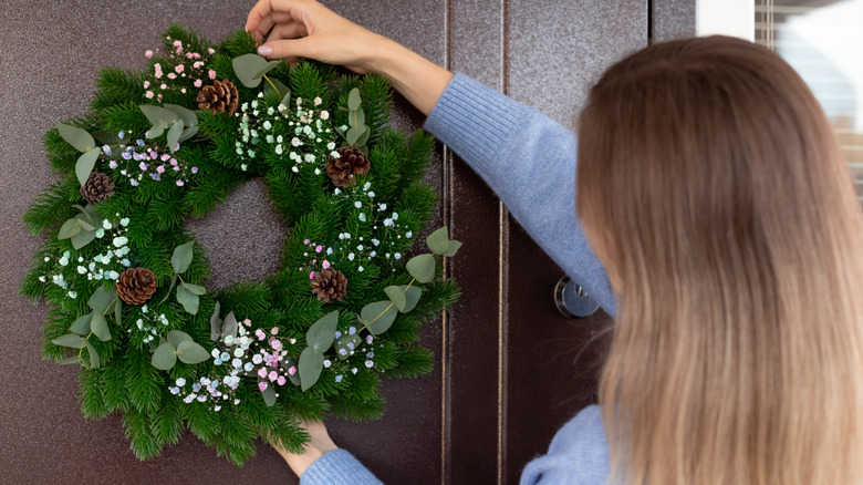 person hanging a Christmas wreath with pine cones on their front door