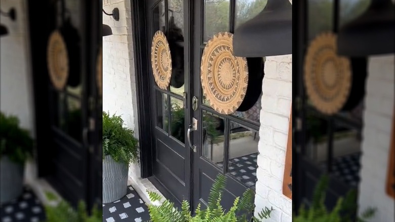 Black double French doors with woven plate decor and a pair of potted plants