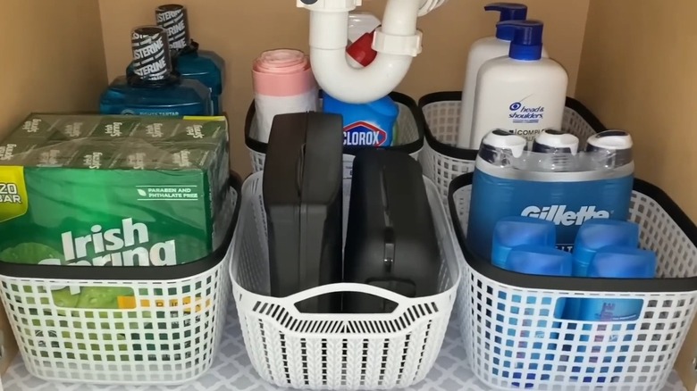 Baskets placed underneath a bathroom sink holding cleaning and bathroom items
