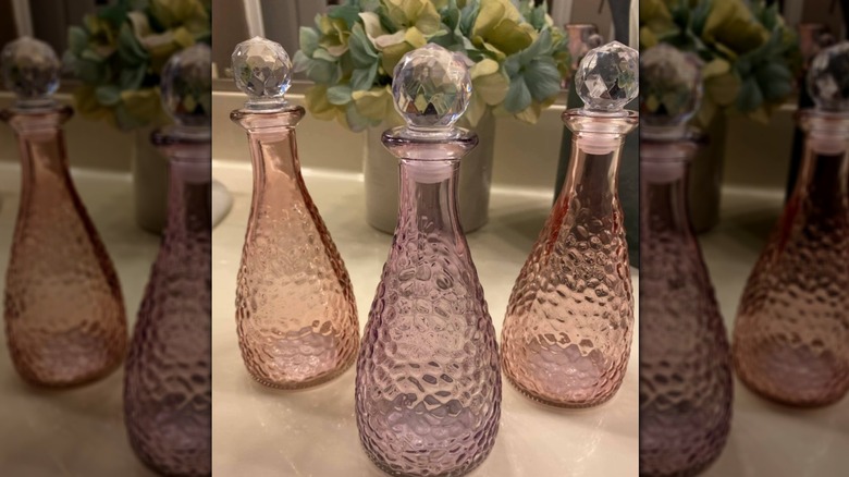 Three different colored glass bottles with stoppers on a bathroom counter