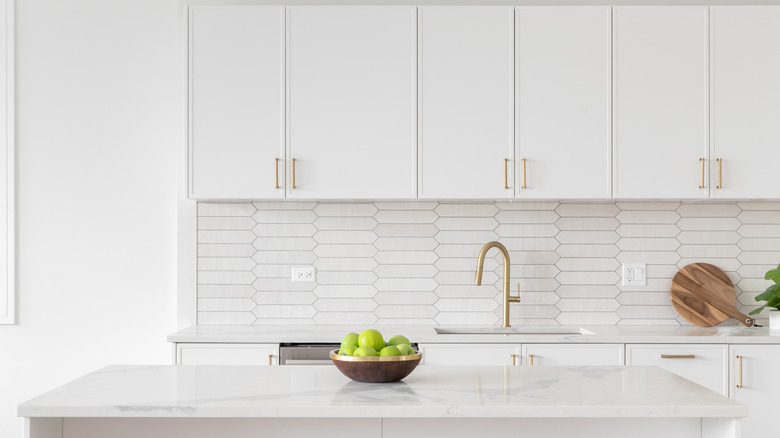 Clean kitchen with white countertops, cabinets, and tiles.