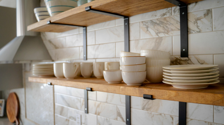 Open kitchen shelves with a collection of white plates and mugs on them