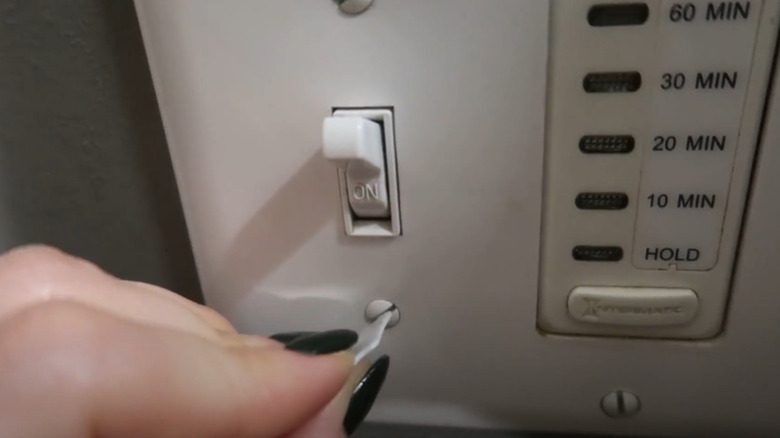 A person unscrewing an light switch cover with a bread tag.
