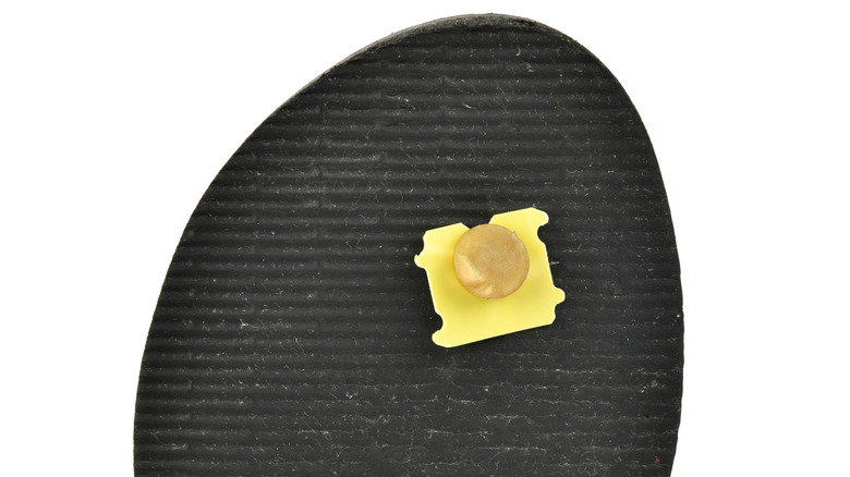 The underside of a flip flop sandal secured by a yellow bread tag.
