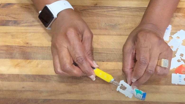 Hands standing a toothbrush on a stand improvised from a bread tag.
