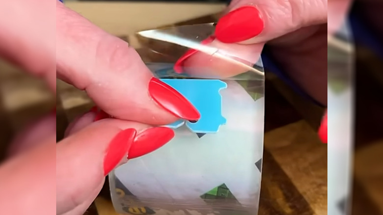 Hands with red nail polish placing a bread tab on the end of a roll of tape.