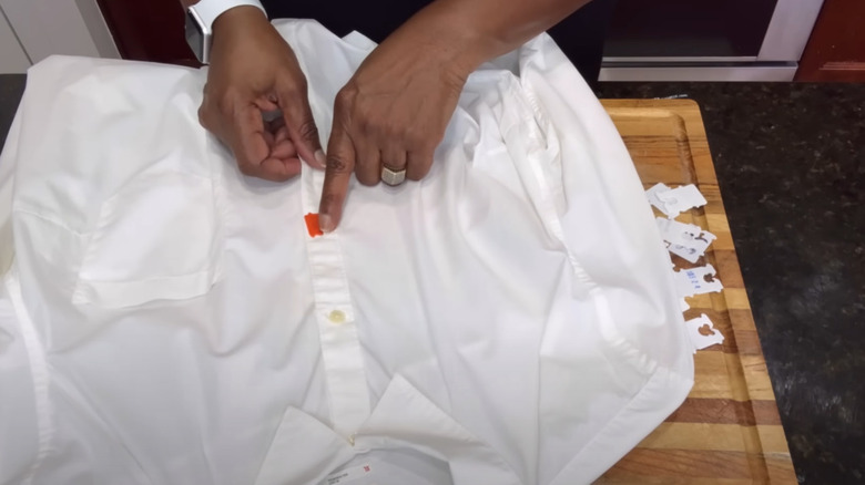 Hands pointing to a bread bag tag being used as a button a white shirt.