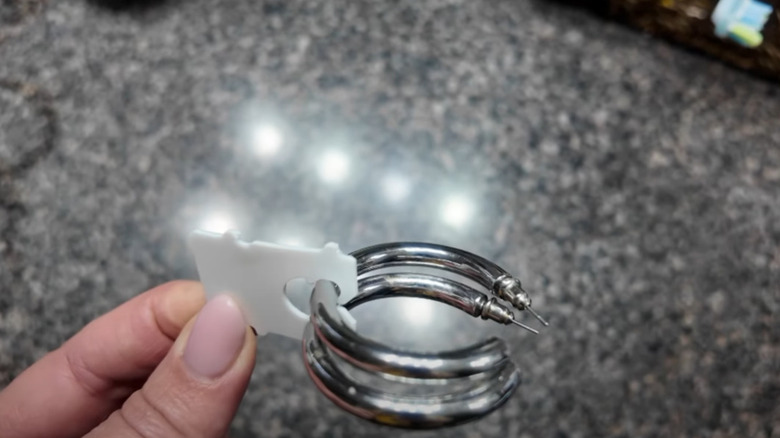 Fingers holding a bread tag with a set of silver hoop earrings threaded through them.