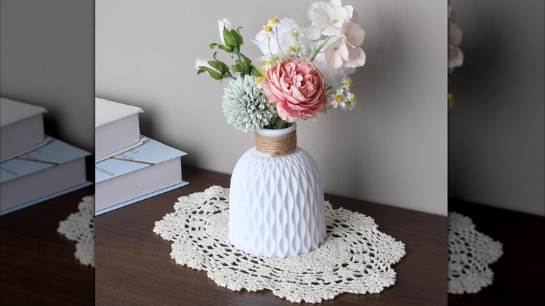Doily on dark wood table beneath unique white vase with spring flower arrangement