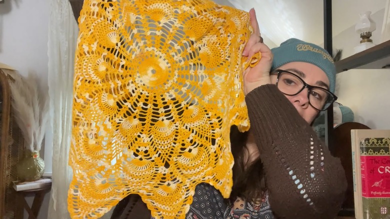 Woman holding up large yellow dyed lace doily at home