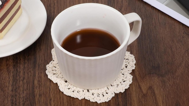 Hot drink on doily coaster on dark wood table with dessert cake nearby