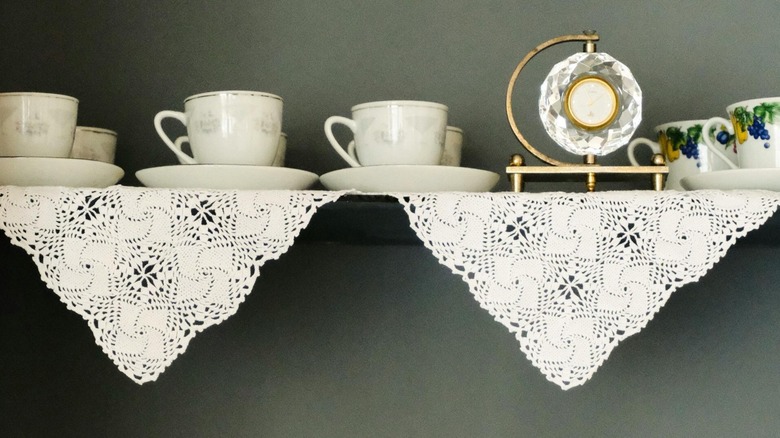Teacups and vintage decor on floating shelf with dangling lace doilies