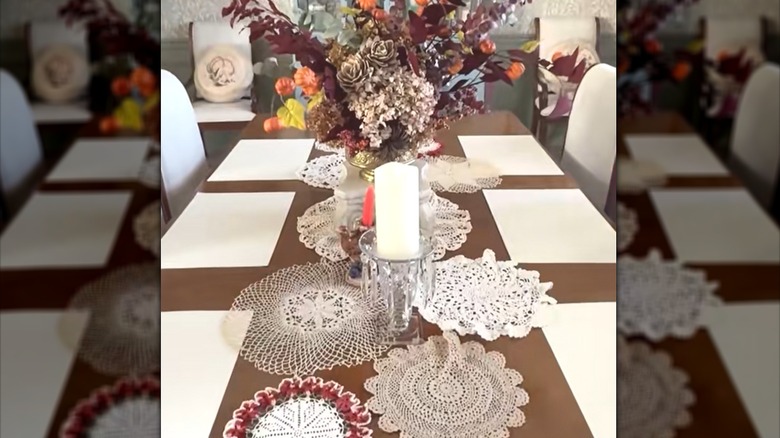 Assorted lacy doilies scattered across middle of long glossy dining table with glamorous centerpieces