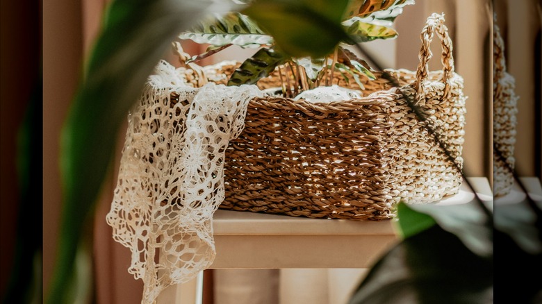 Decorative woven basket with doily hanging off the side behind potted houseplant