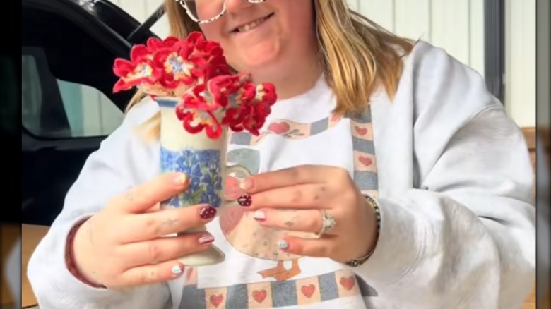 Young woman holding up small vintage vase with red and white doily tucked inside