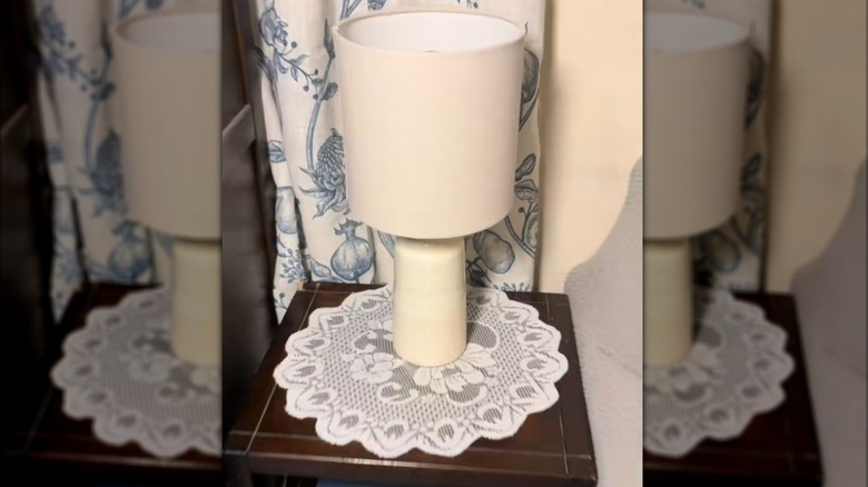 Traditional doily beneath white lamp in old-fashioned room with patterned curtains