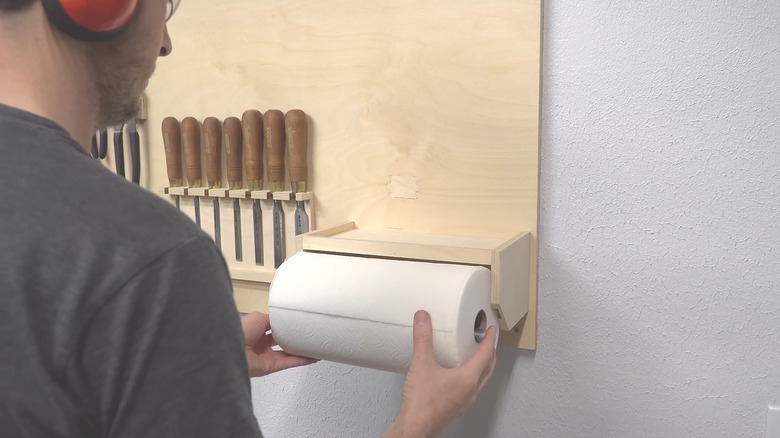 Man hooking paper towel roll on DIY wooden tool storage