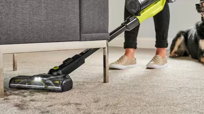 A woman using a cordless vacuum to clean under a sofa