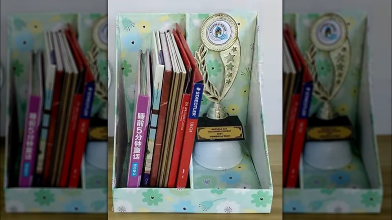Floral desk stand with hobby books and trophy on wood shelf.