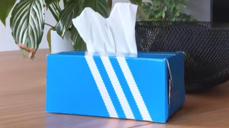 Blue Adidas shoebox with white stripes repurposed as tissue dispenser.