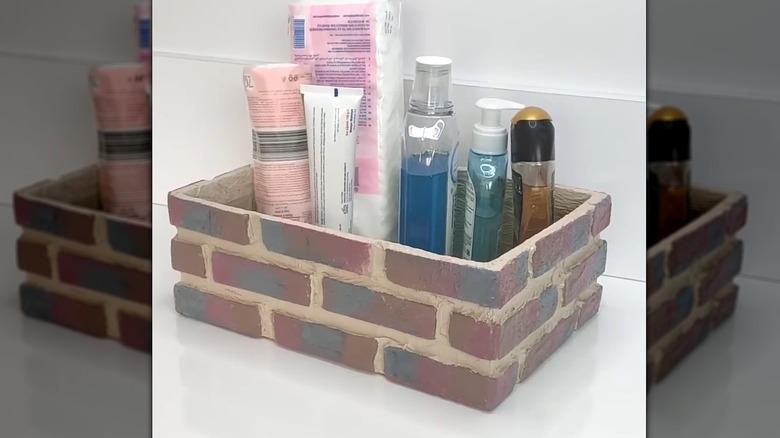 Bathroom essentials and bottles in brick-style organizer on white countertop.