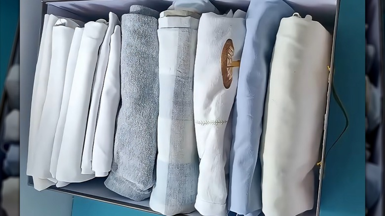 Folded garments, linens, and washcloths lined up in shoebox.