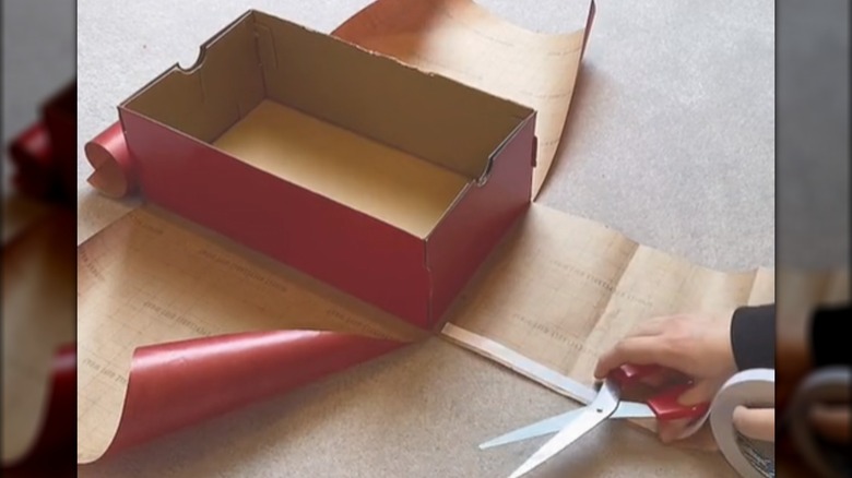 Woman wrapping a shoebox with red paper.