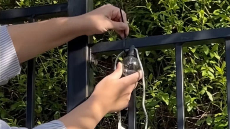 Person hanging string lights on metal fence with zip ties