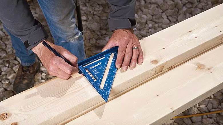 An overhead shot of a person using a blue rafter square to mark cuts on a piece of lumber