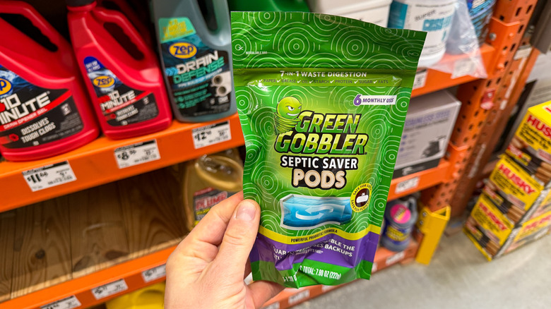 A person holds a pack of Green Gobbler Septic Saver Pods near an orange shelf at Home Depot