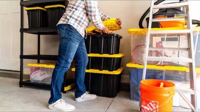 A person places items on top of three stacked black storage totes in a garage