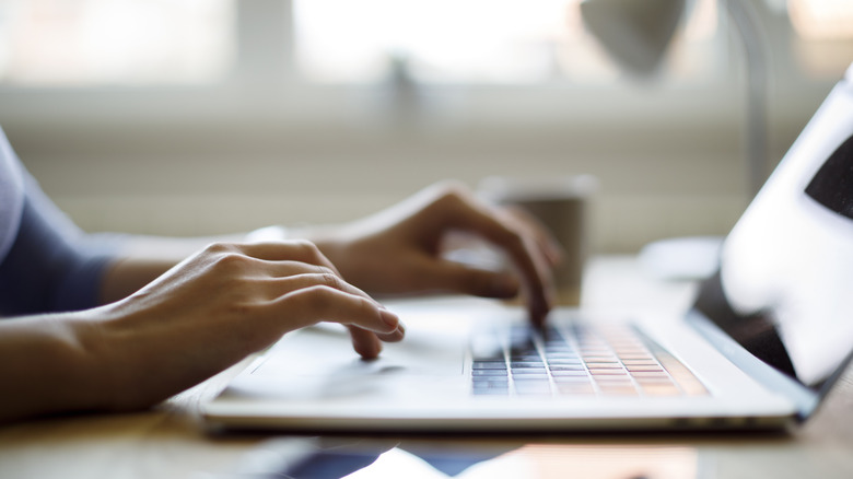 A woman's hands type on a laptop