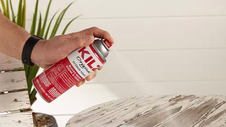 A person sprays KILZ Original Spray Paint on an old white table