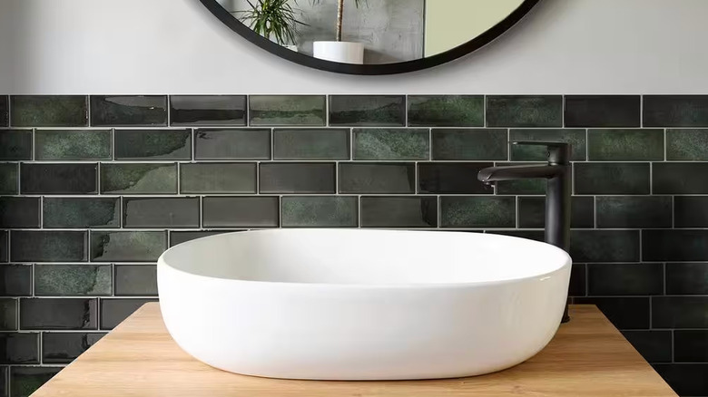 Dark green peel-and-stick tiles are installed behind a modern white bathroom sink