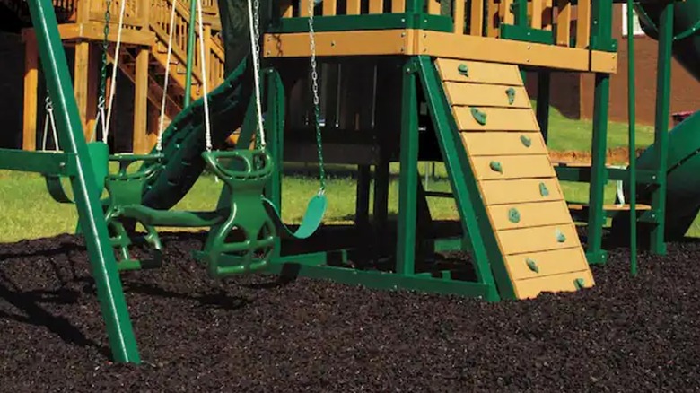 Brown rubber mulch pads the ground under a green playground