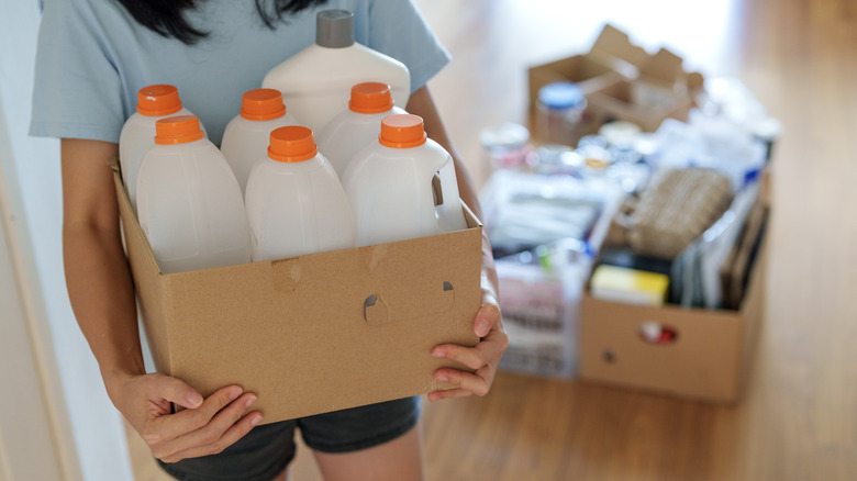 Woman carrying box filled with half-gallon milk jugs