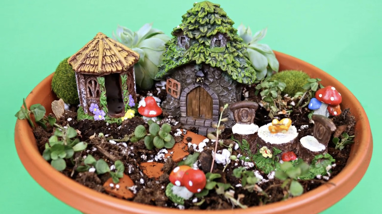 Two decorative Dollar Tree fairy houses surrounded by small plants in a terracotta planter