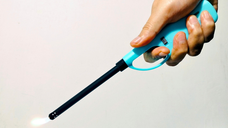 A person's hand using a long multi-purpose lighter