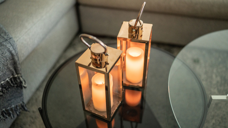 Two golden candle lanterns sitting on a glass coffee table