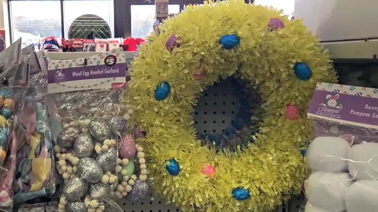 A yellow tinsel wreath decorated with glitter eggs hanging on a Dollar Tree shelf
