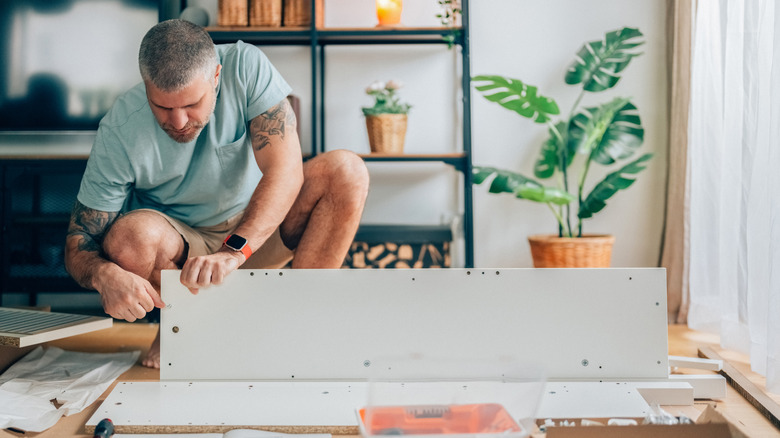 Man squatting and assembling shelf in brightly lit modern room