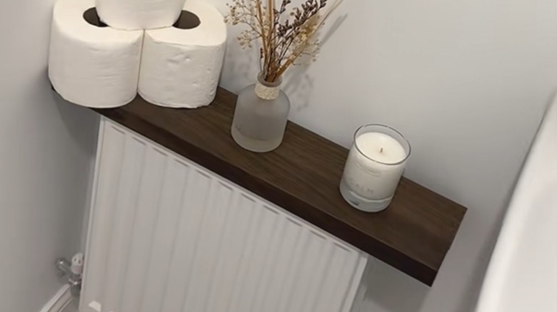 Dark brown IKEA picture ledge folded over inactive radiator with bathroom essentials on top