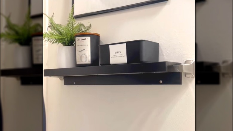 Black IKEA picture ledge tucked over towel rod with bathroom plant, wipes, and candle