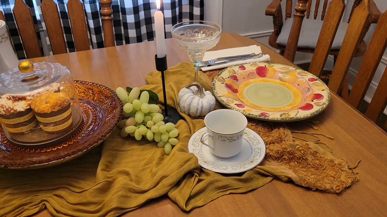 Rumpled gold scarf on wood dining table with decorations and table setting