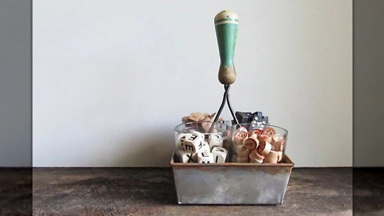 An upcycled bread pan holding dice, dominoes, and other game pieces.