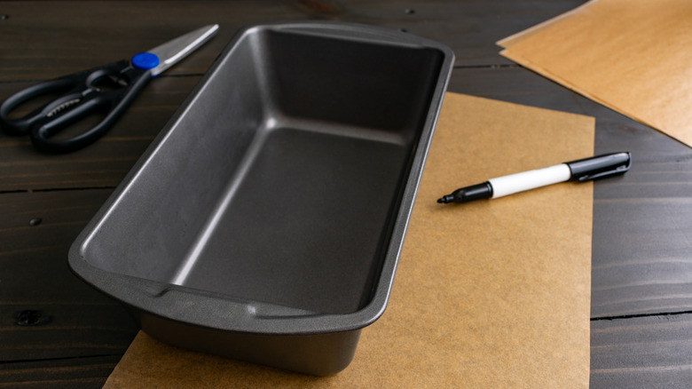 Empty bread loaf pan with paper, scissors, and pen around it
