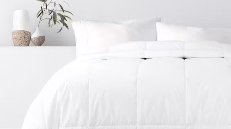 A duvet insert is draped on a mattress in an all-white bedroom